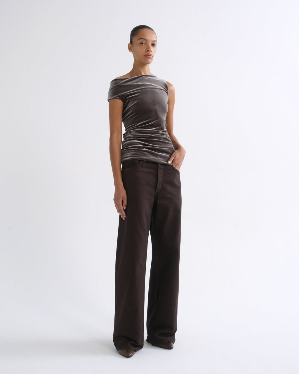 Woman wearing a brown striped sleeveless top with dark brown wide leg pants on a grey background.