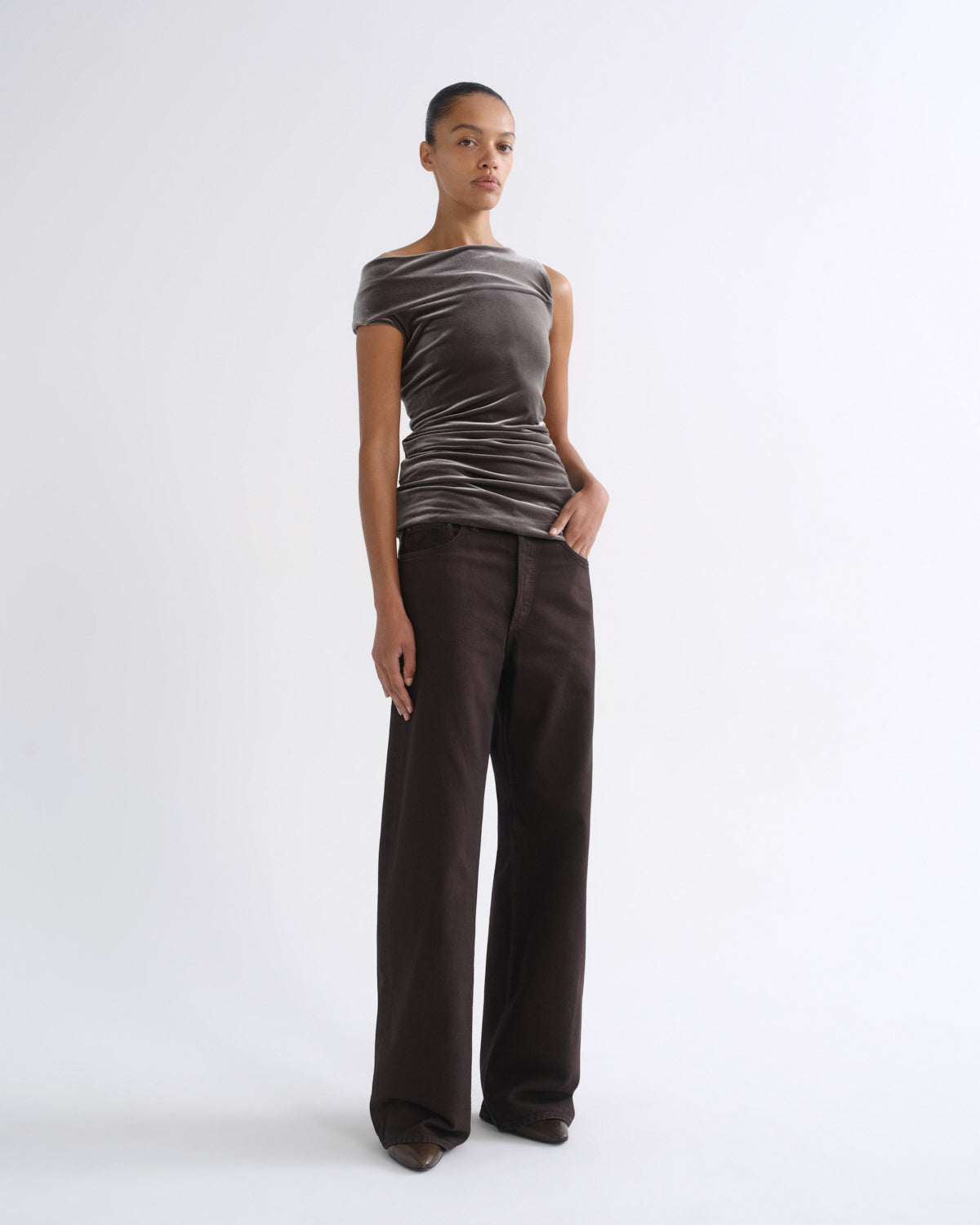 Woman wearing a brown striped sleeveless top with dark brown wide leg pants on a grey background.