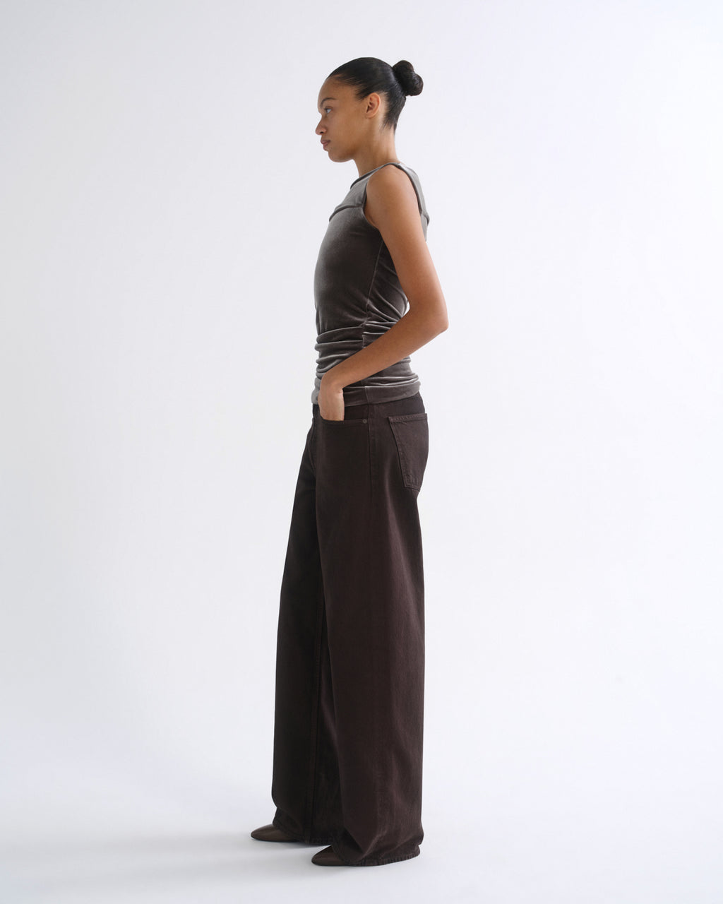 Woman wearing a brown striped sleeveless top with dark brown wide leg pants viewed from the side on a grey background.