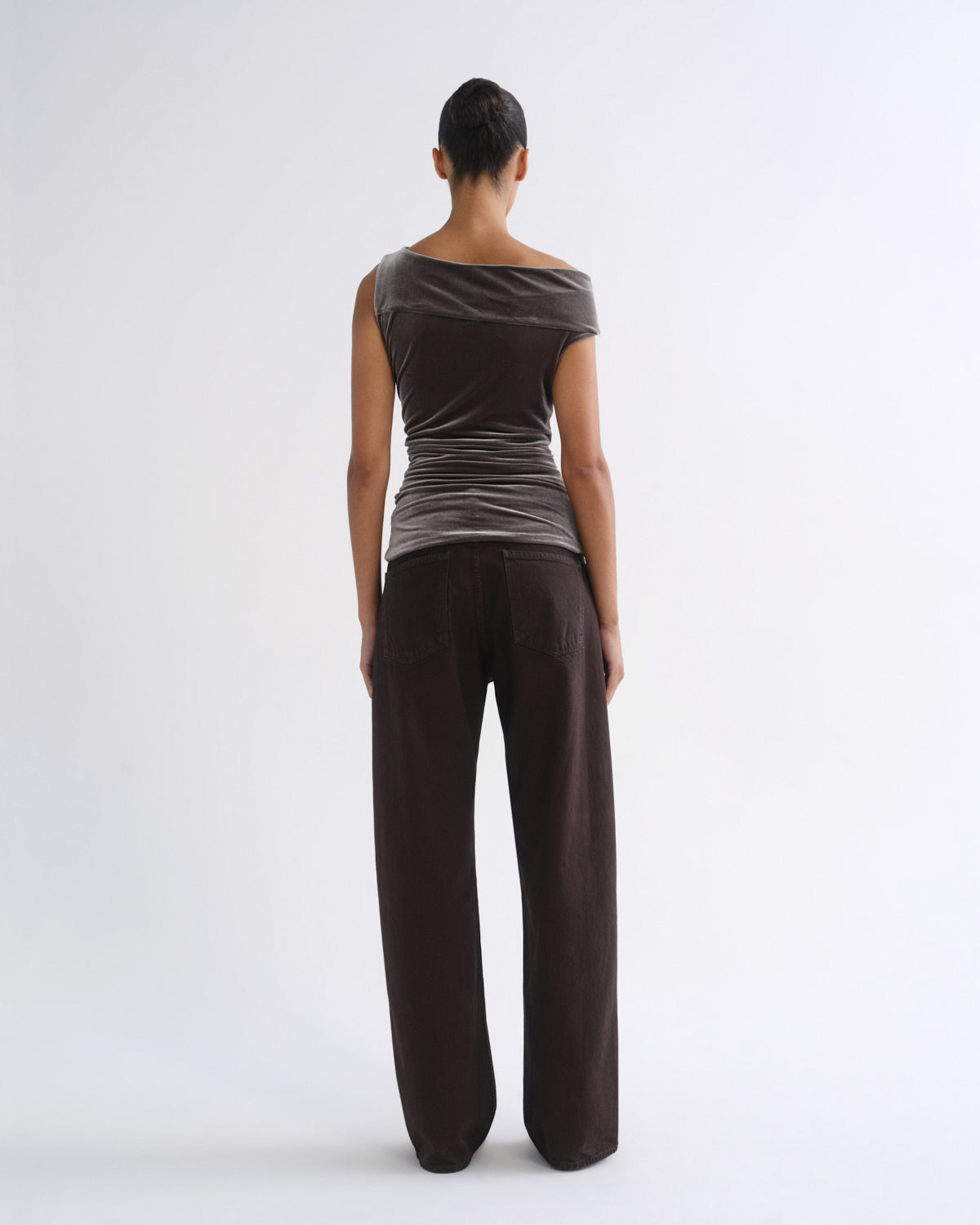 Woman wearing a brown striped sleeveless top with dark brown wide leg pants viewed from the back on a grey background.