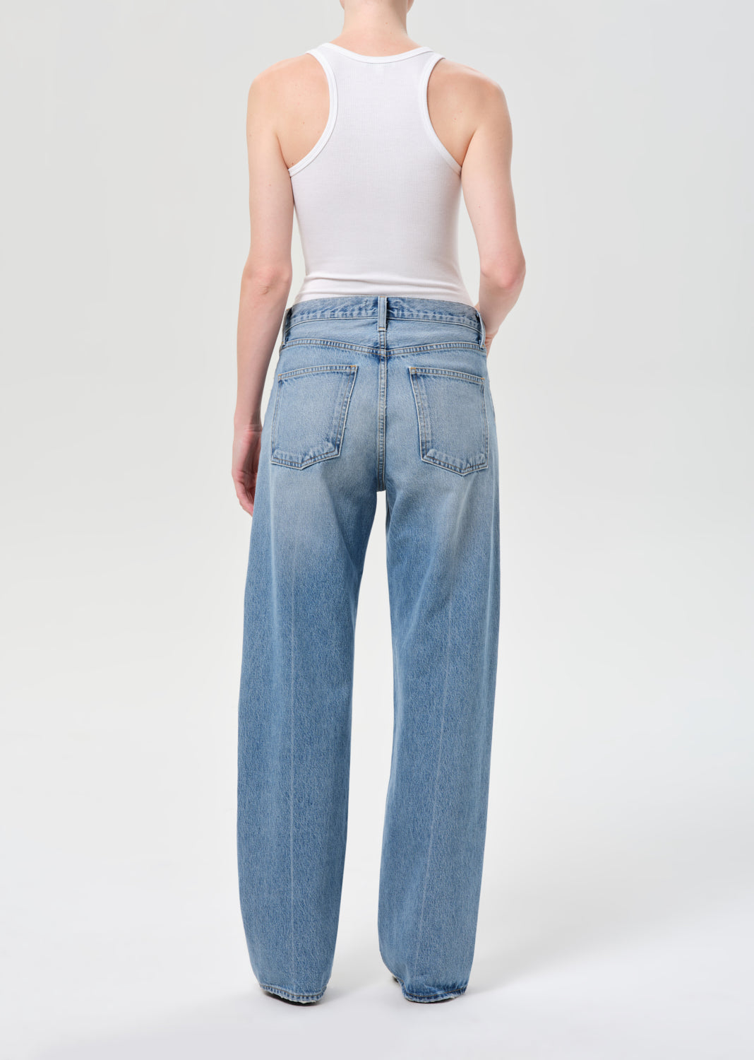 Person wearing light blue jeans and a white tank top on a white background