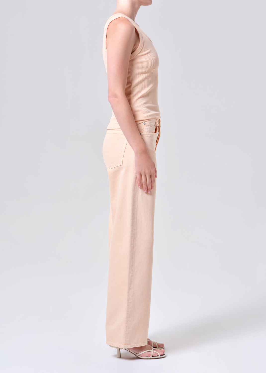 Person wearing a beige sleeveless top and wide-leg pants on a white background