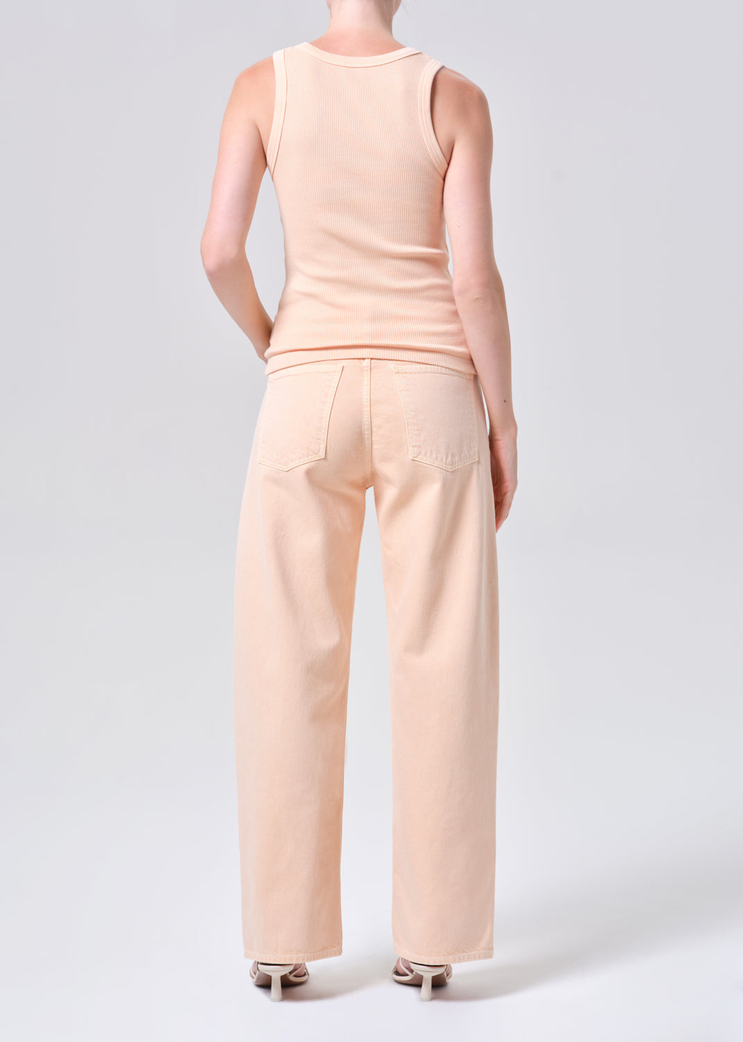 Person wearing a beige sleeveless top and wide-leg pants on a white background
