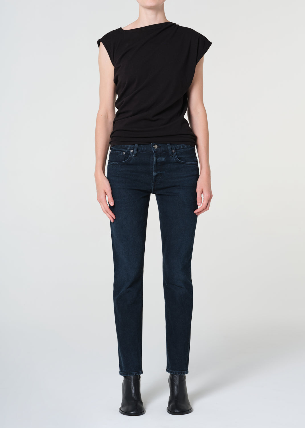 Person wearing a black sleeveless top and dark blue jeans on a white background