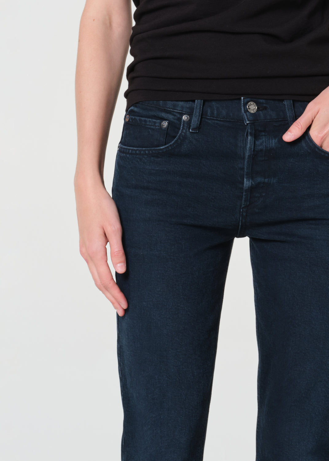 Person wearing dark blue jeans and a black top on a light gray background