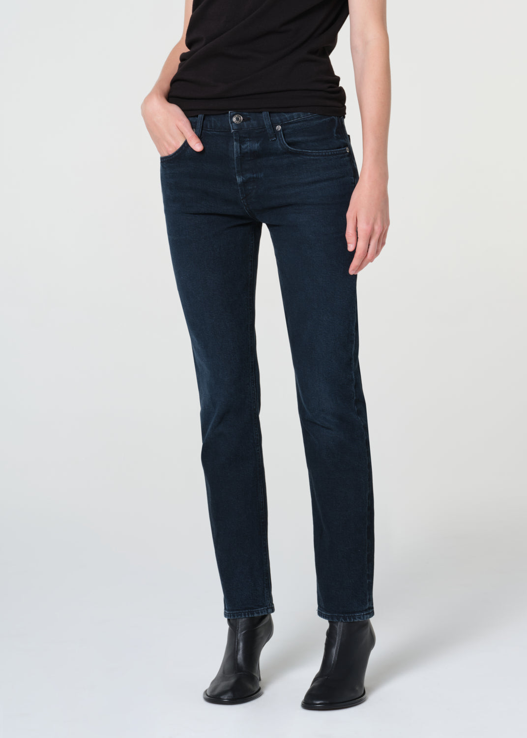 Person wearing dark blue jeans and black boots on a white background
