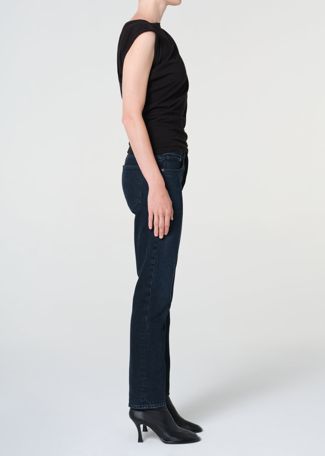 Person wearing a black sleeveless top and dark jeans on a white background