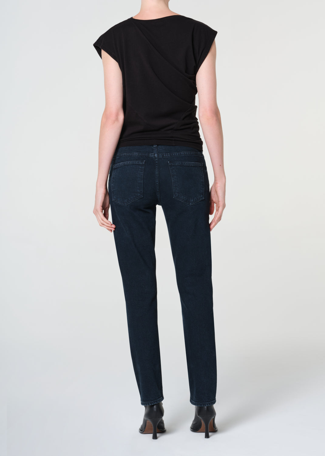Person wearing a black top and dark jeans on a white background