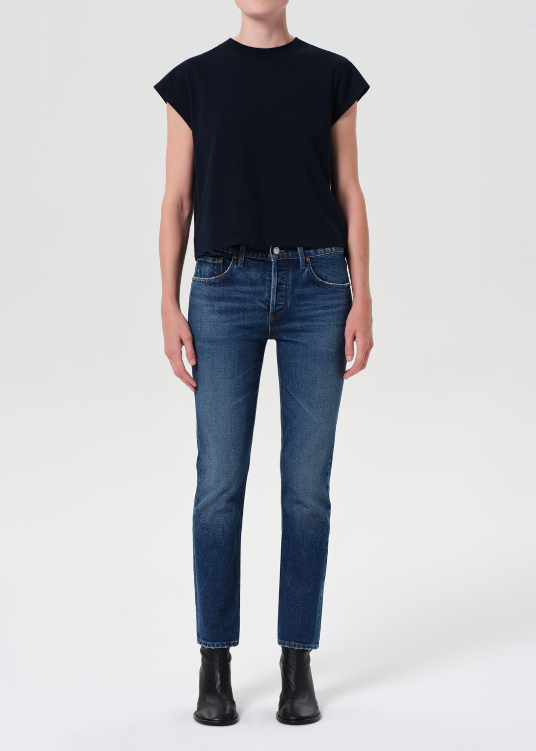 Person wearing a black sleeveless top and blue jeans on a white background