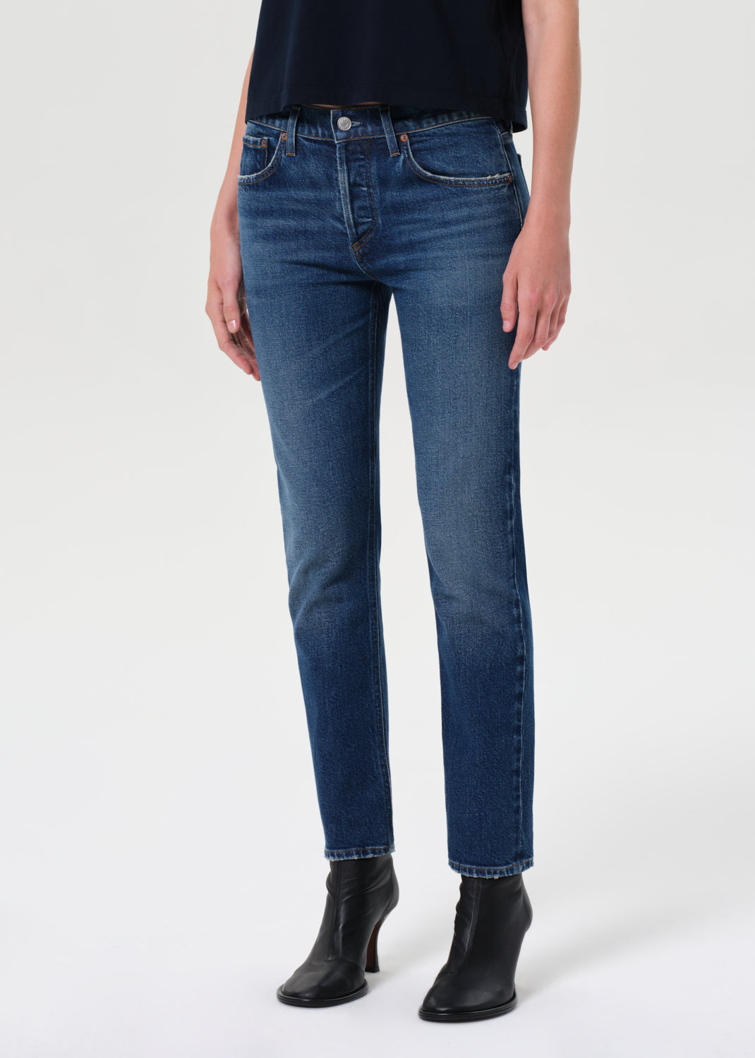 Person wearing blue jeans and black boots on a white background