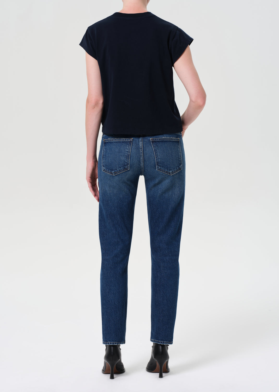 Person wearing blue jeans and a black top on a white background
