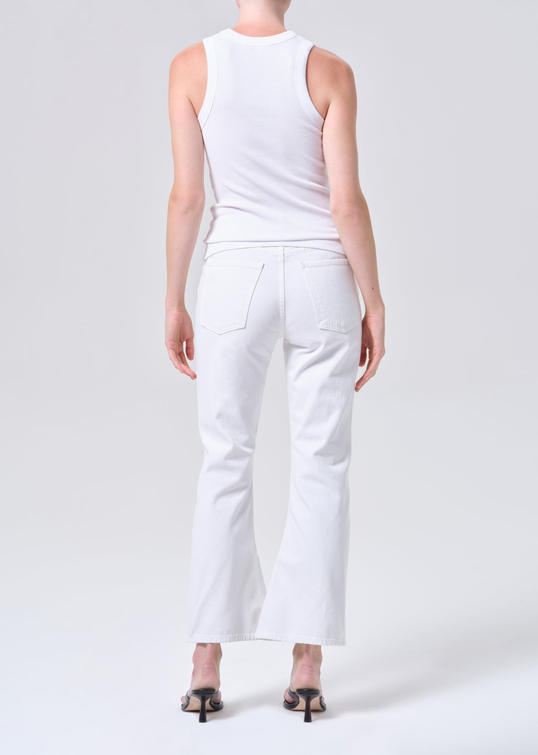 Person wearing a white sleeveless top and white pants on a light gray background