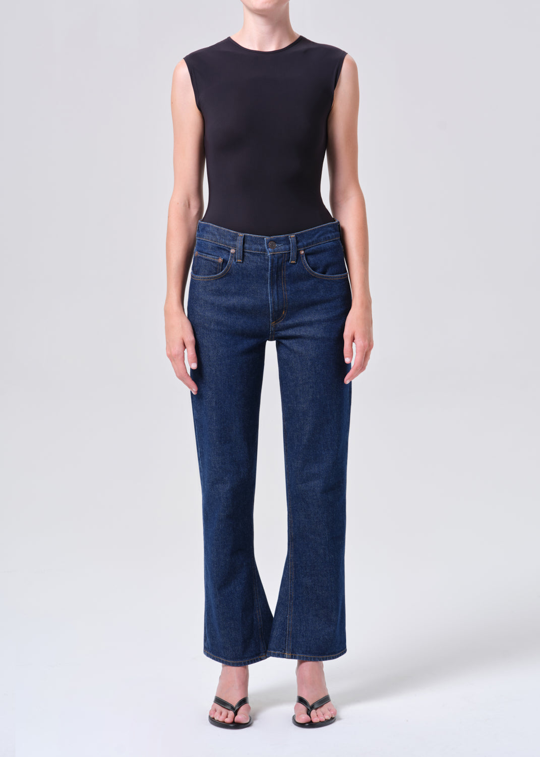 Person wearing a black sleeveless top and dark blue jeans on a white background