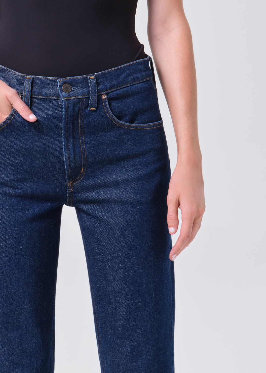 Person wearing dark blue jeans on a plain background