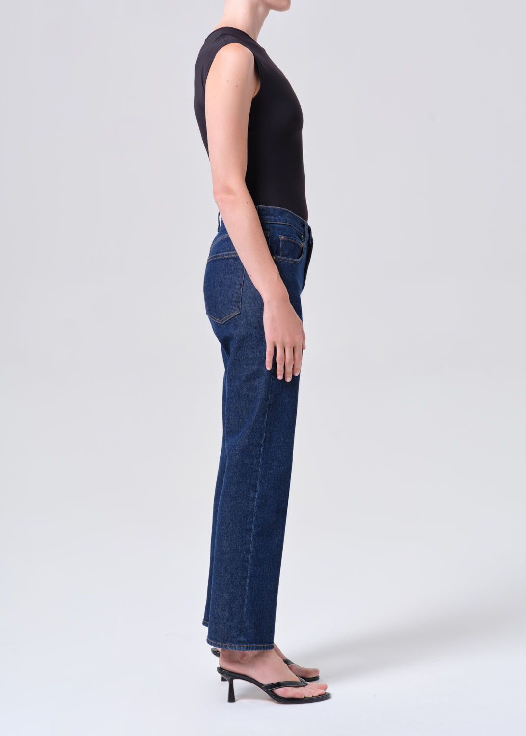 Person wearing blue jeans and a black top on a white background