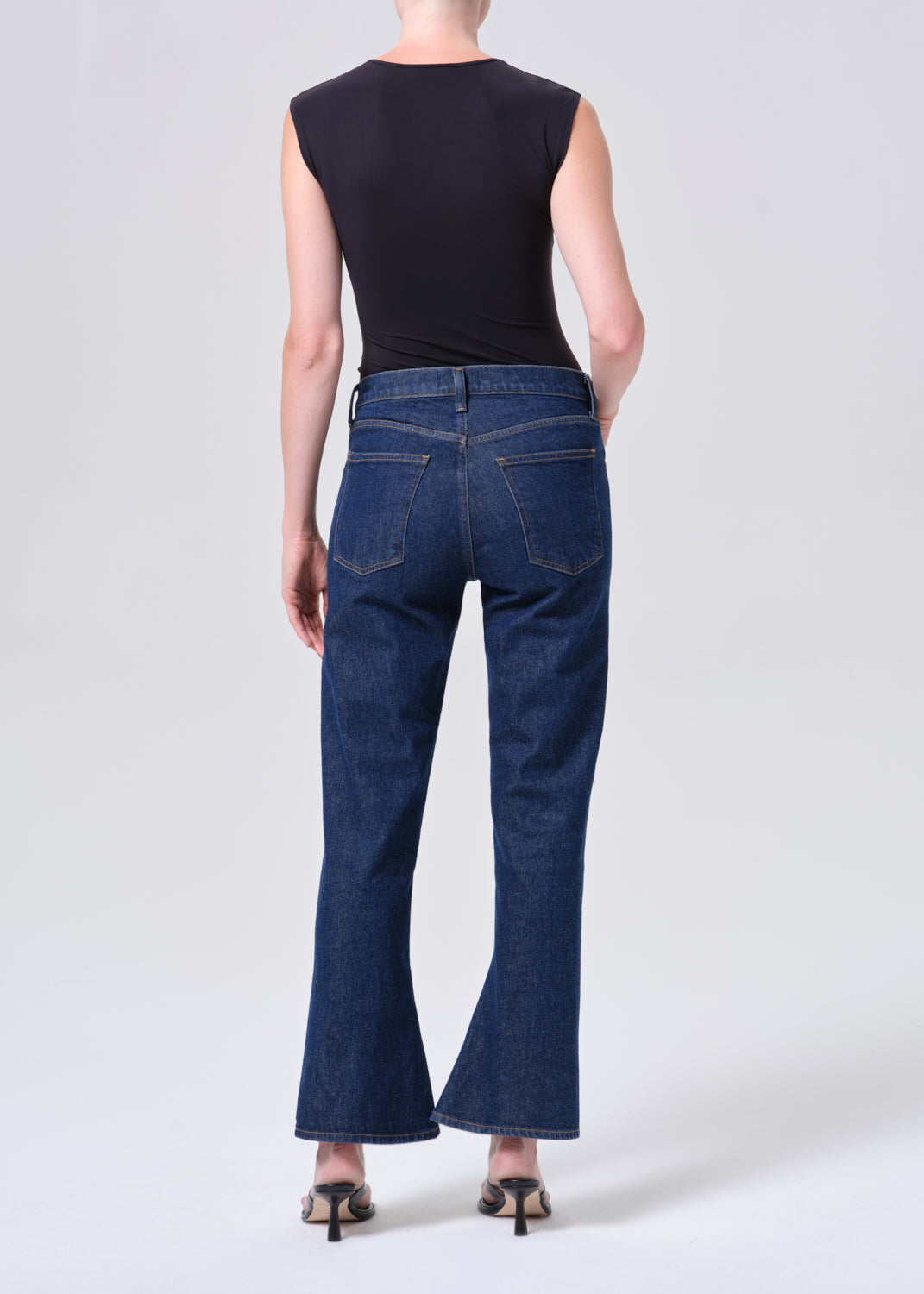 Person wearing blue jeans and a black sleeveless top on a white background