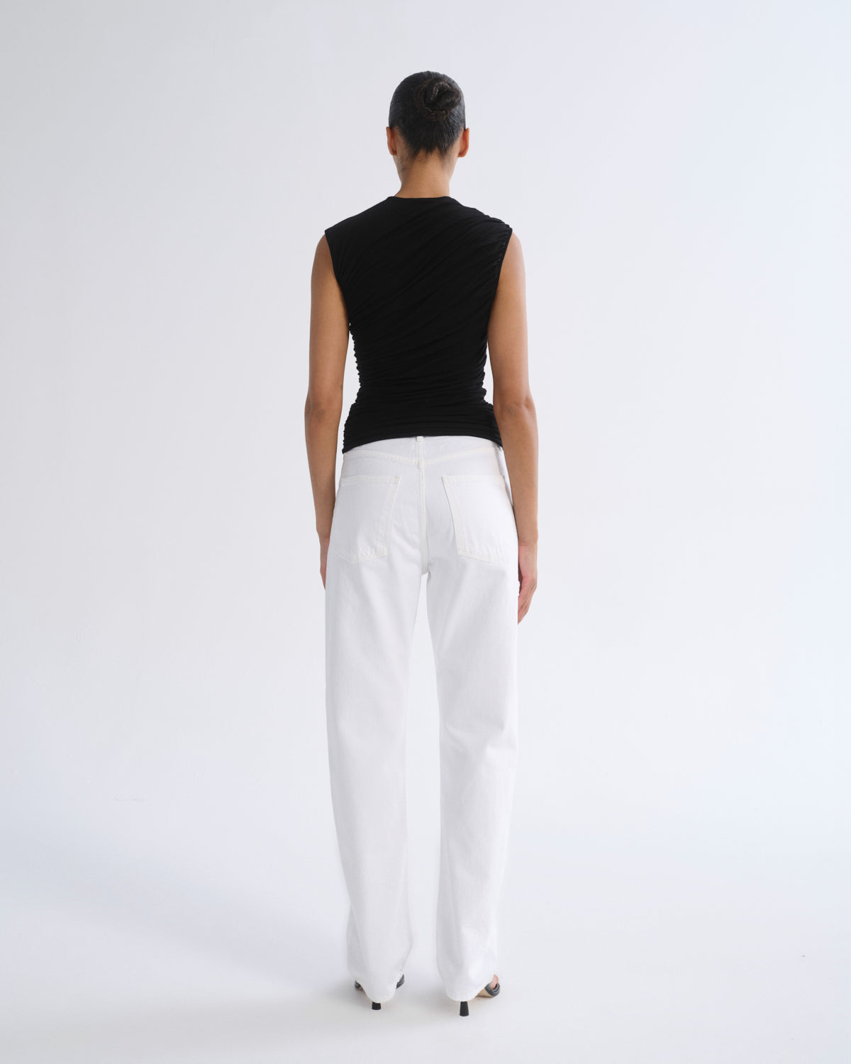 A model shown from the back wearing a black sleeveless top and white wide-leg pants against a plain white studio background.