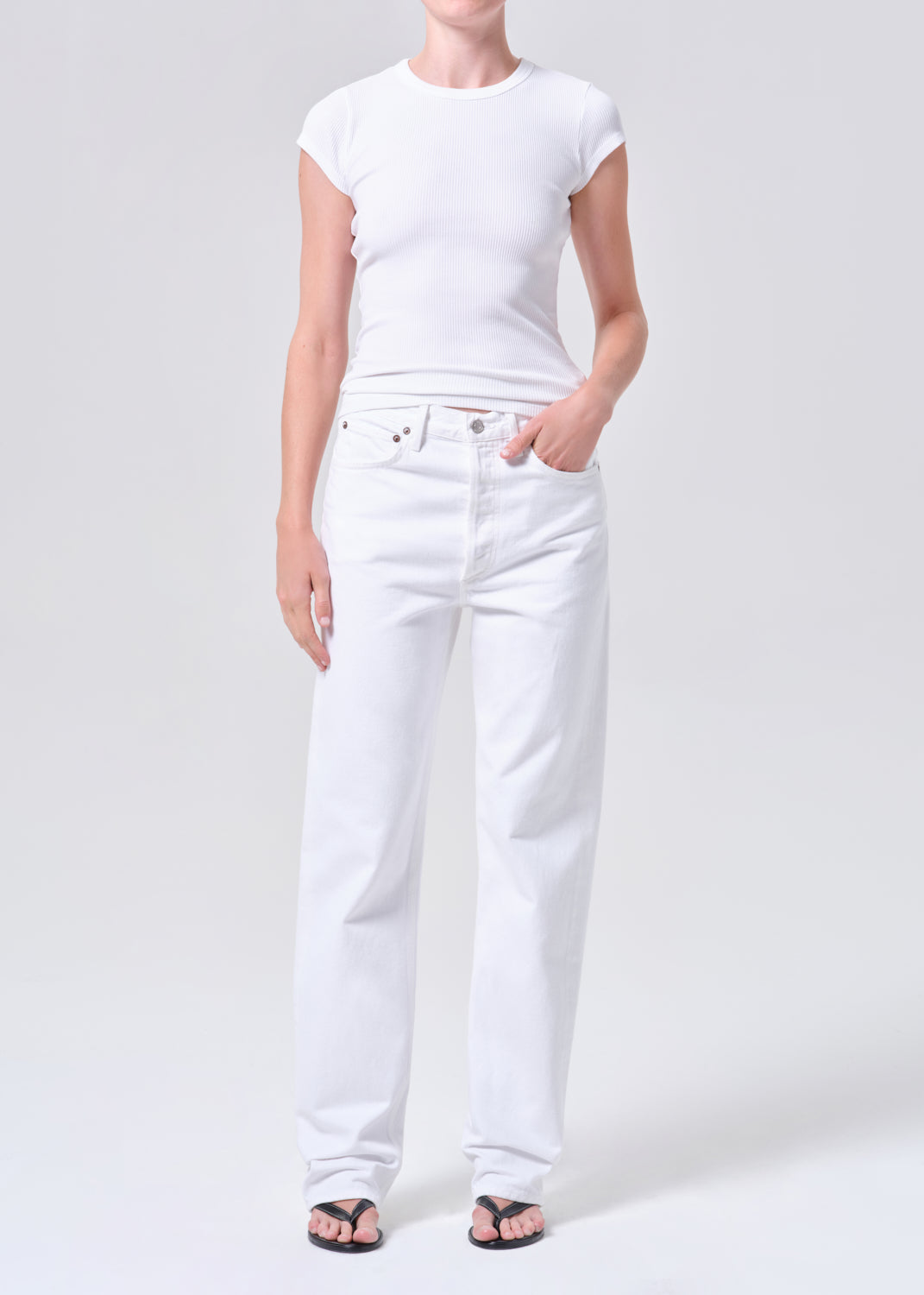 Person wearing a white t-shirt and white jeans on a light gray background