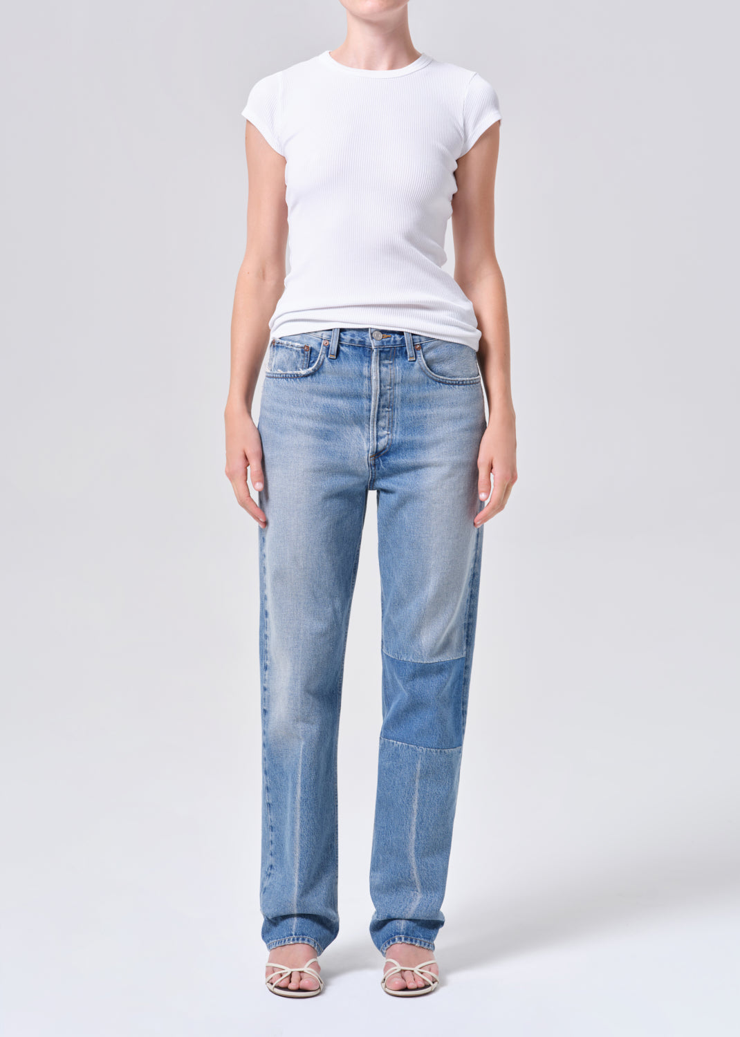 Person wearing light blue jeans and a white t-shirt on a plain background