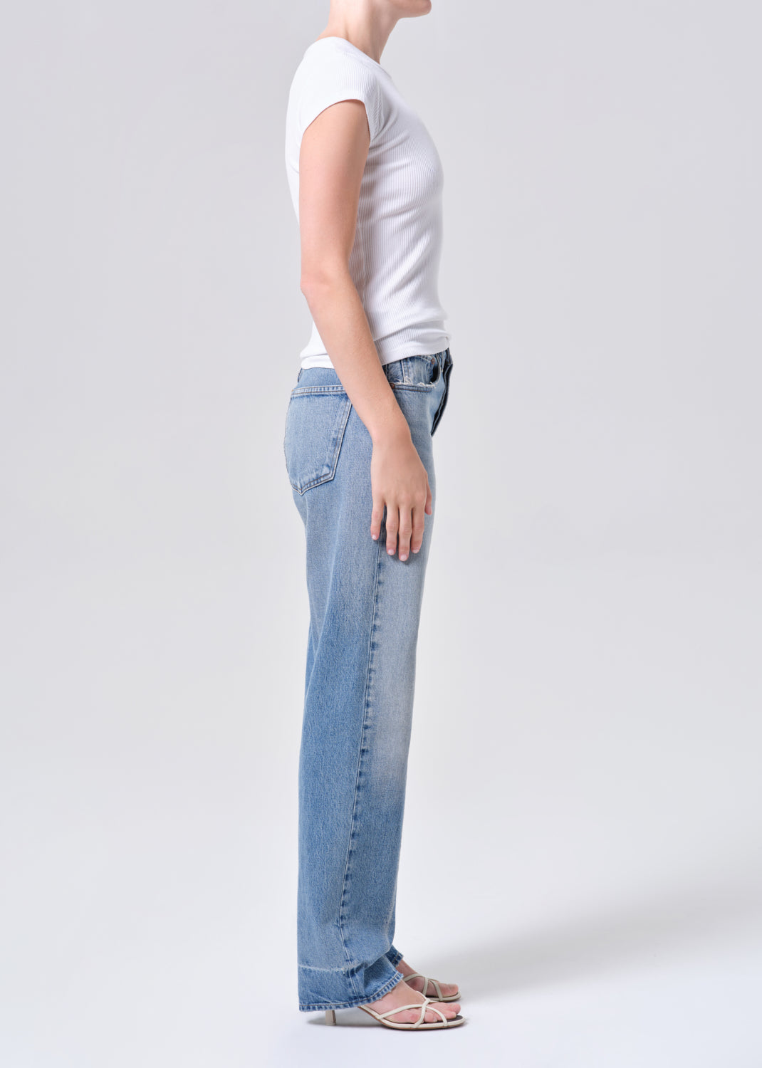 Person wearing light blue jeans and a white t-shirt on a plain background