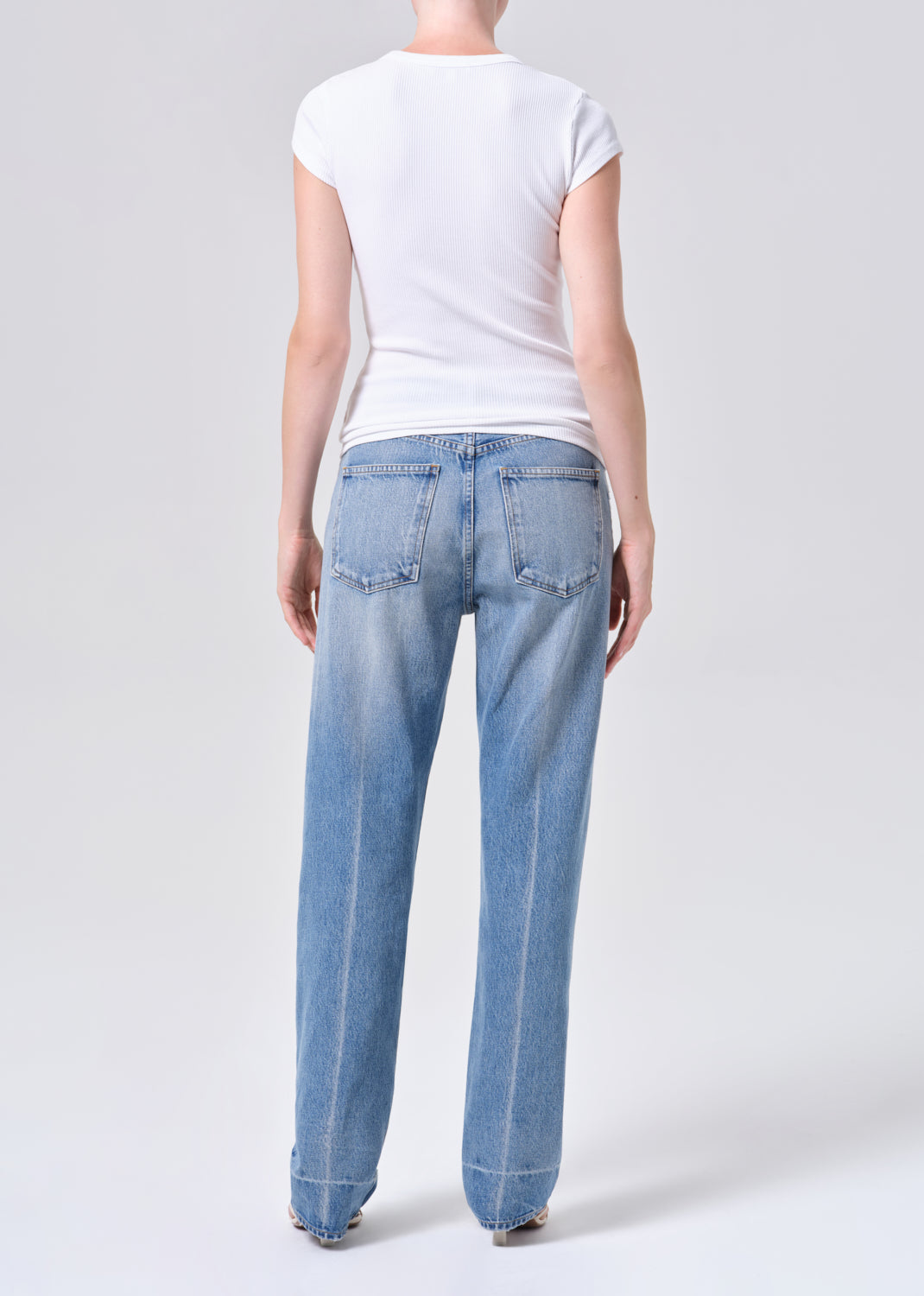 Person wearing light blue jeans and a white t-shirt on a plain background