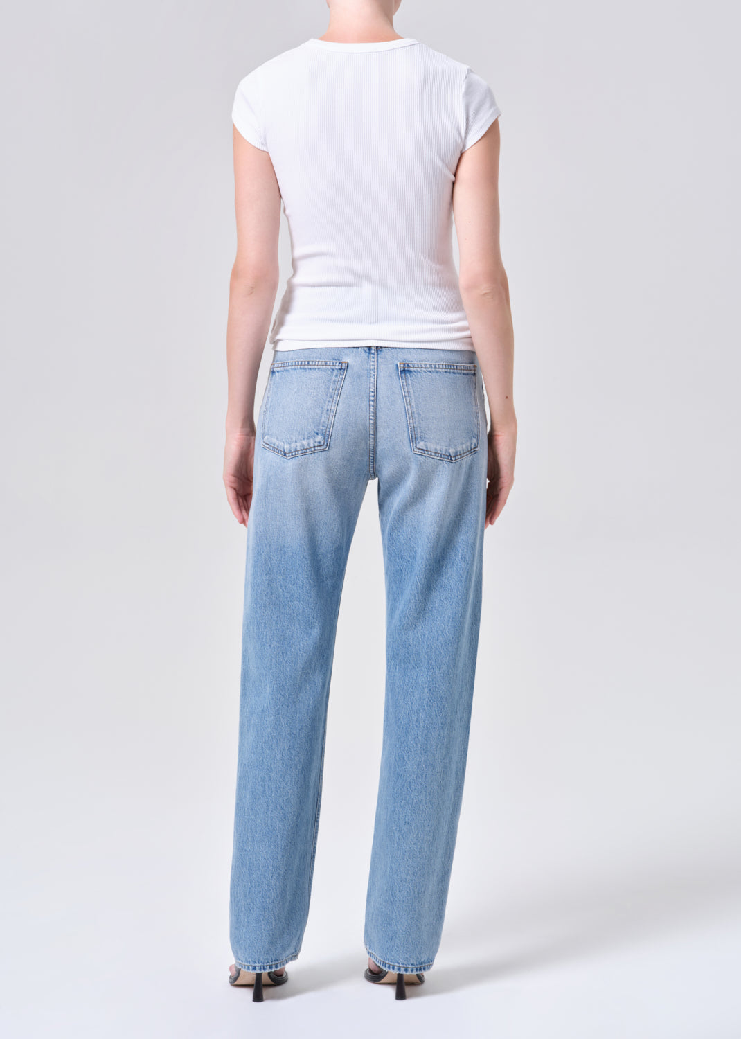 Person wearing light blue jeans and a white t-shirt on a plain background