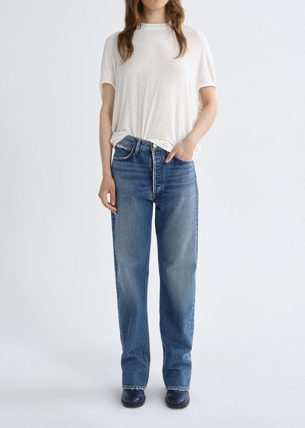 Person wearing a white short sleeve crewneck tee with light wash straight leg jeans on a white background