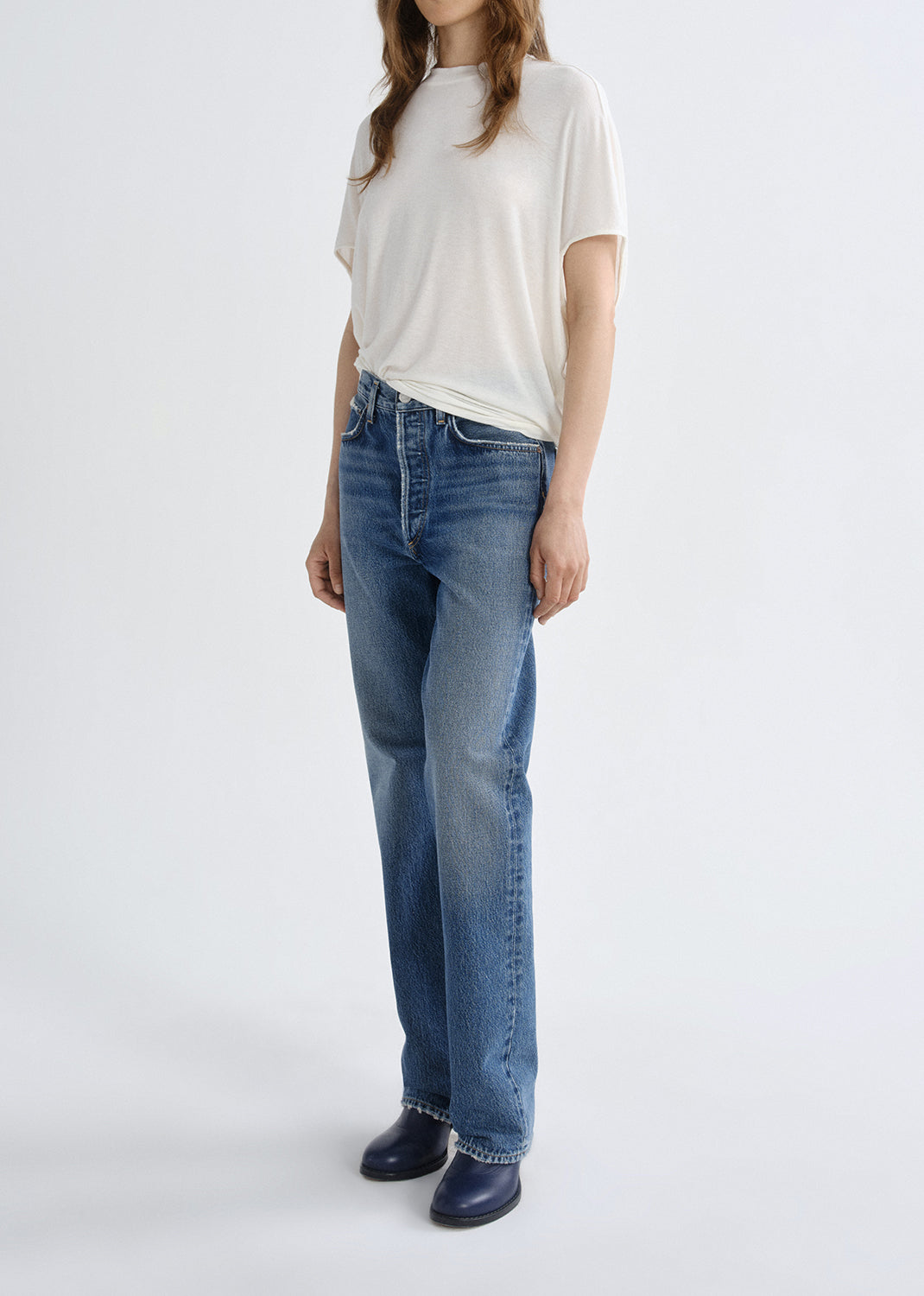 Person wearing a white short sleeve crewneck tee with light wash straight leg jeans viewed from the side on a white background