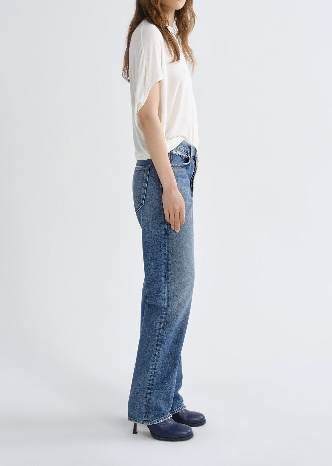 Person wearing a white short sleeve crewneck tee with light wash straight leg jeans viewed from the side on a white background