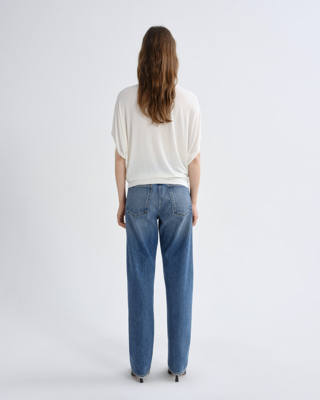 Person wearing a white top and blue jeans on a light gray background