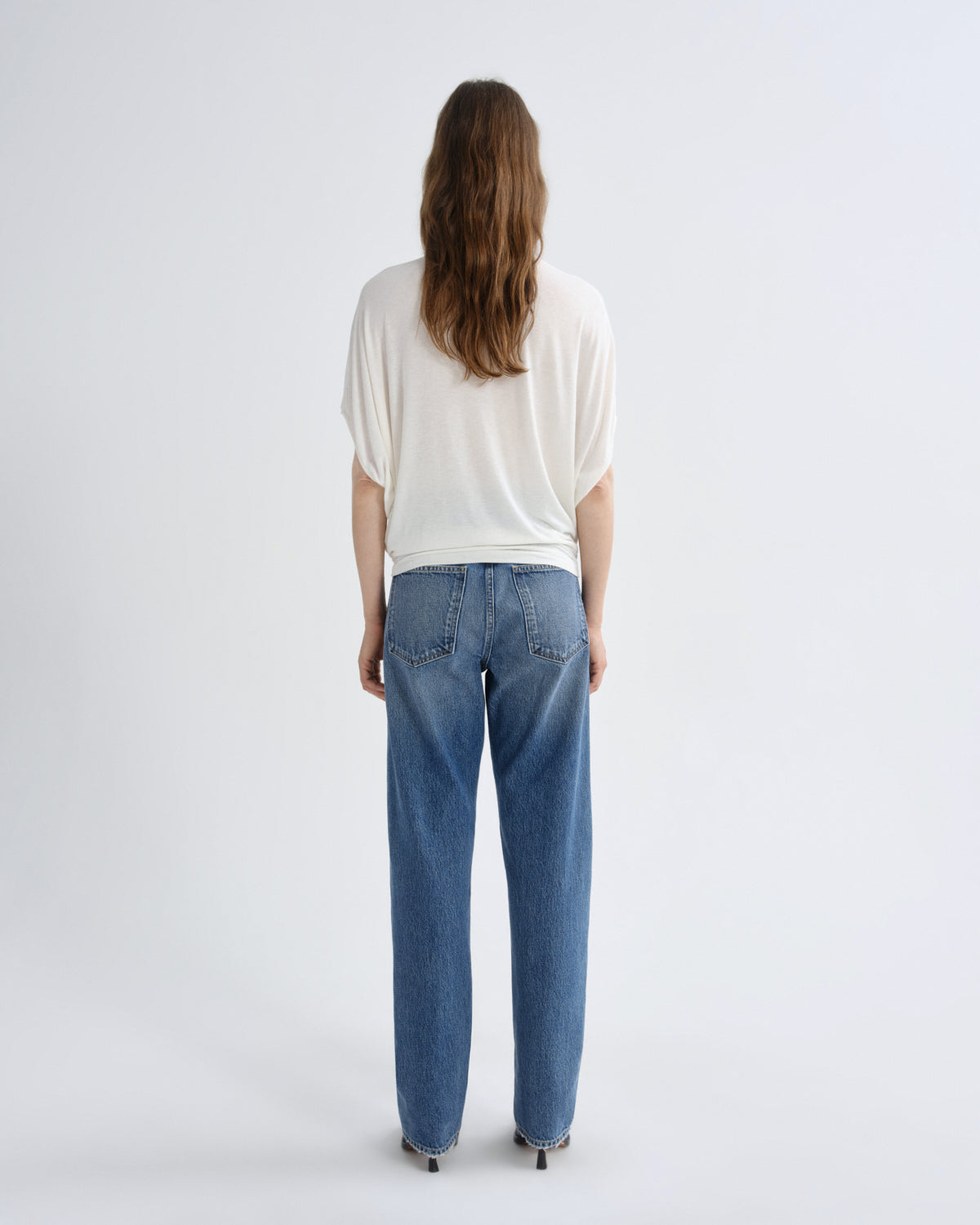 Person wearing a white top and blue jeans on a light gray background
