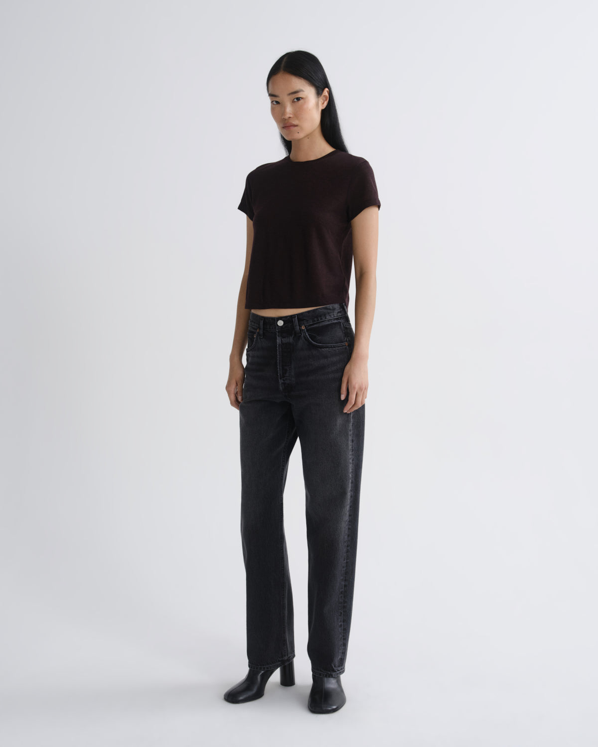 Woman wearing a black t-shirt and dark jeans on a white background