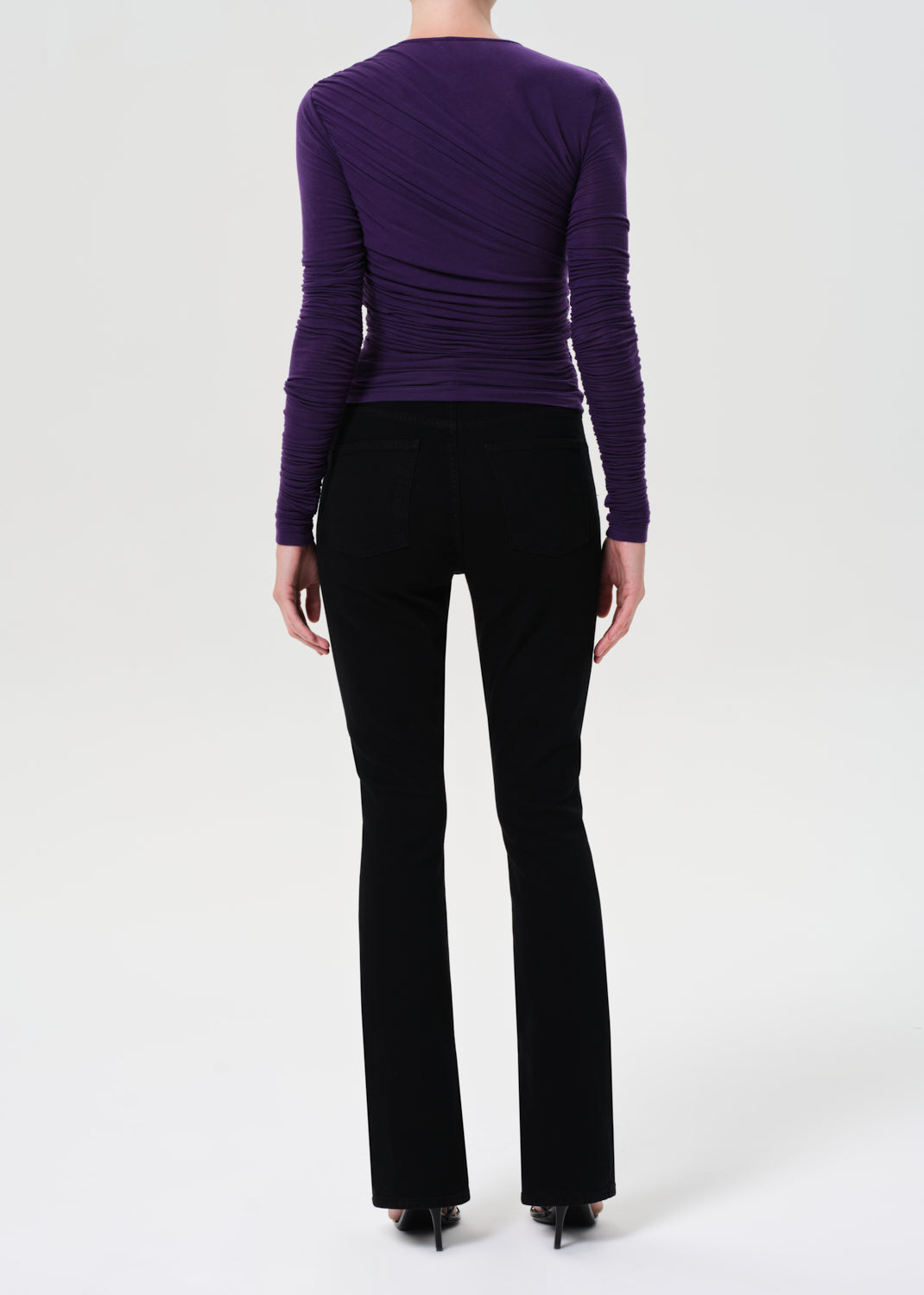 Person wearing a purple long-sleeve top and black pants on a white background