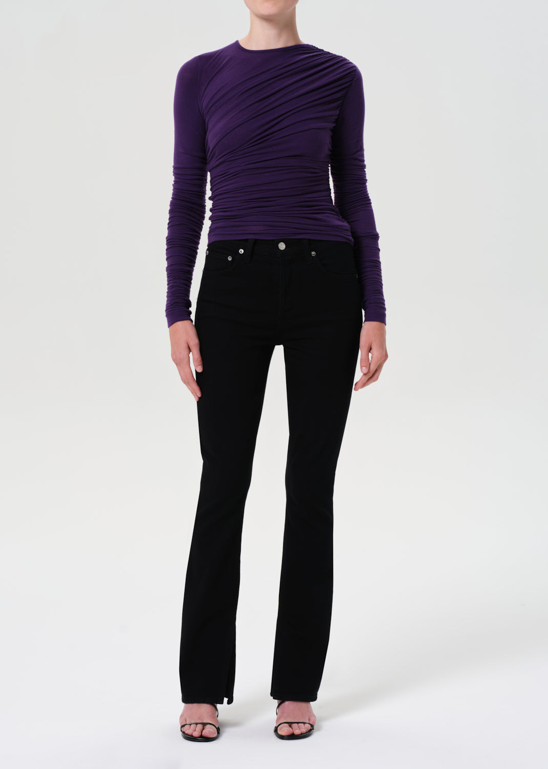 Person wearing a purple long-sleeve top and black pants on a white background