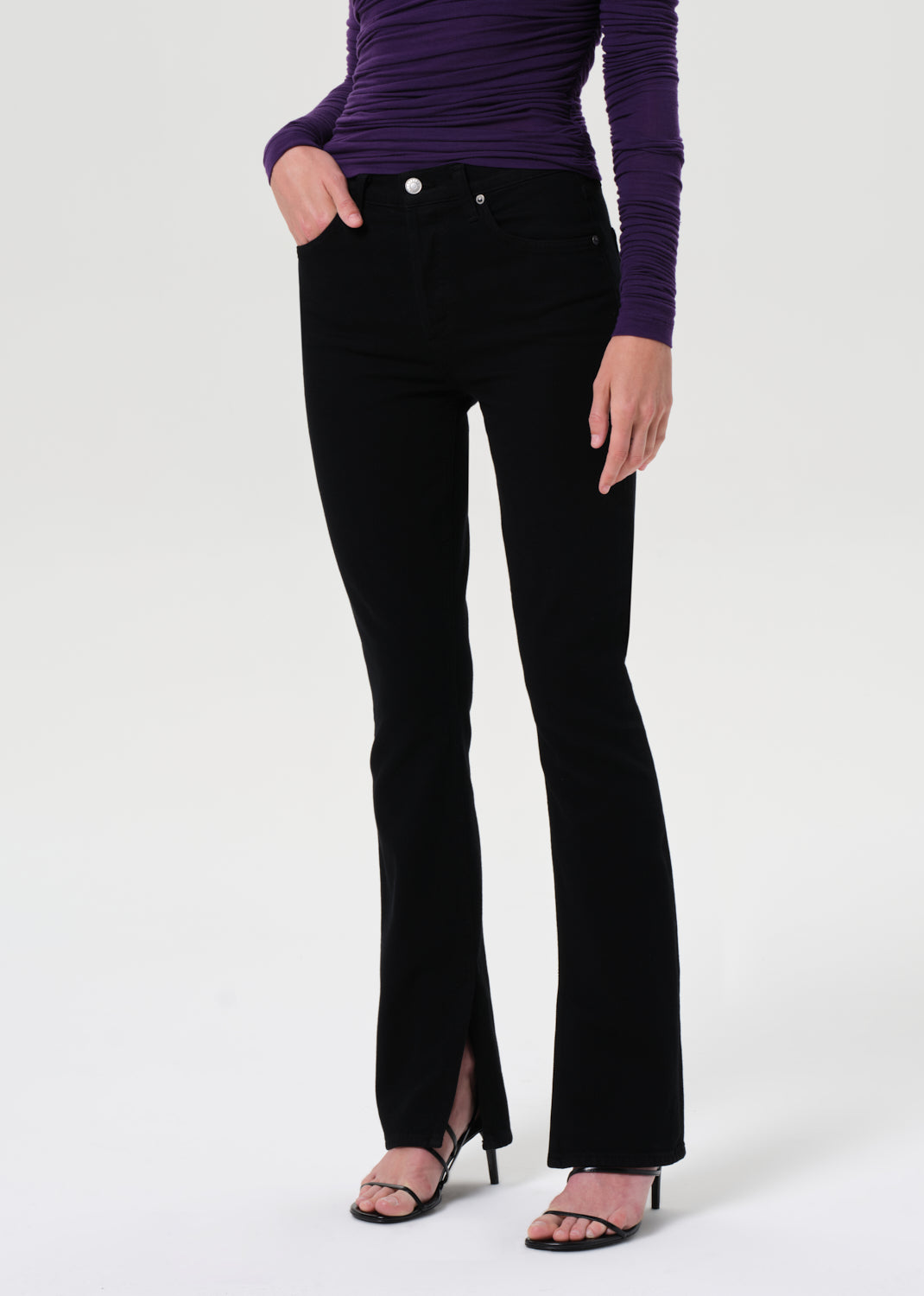 Person wearing black flared jeans and a purple top on a white background