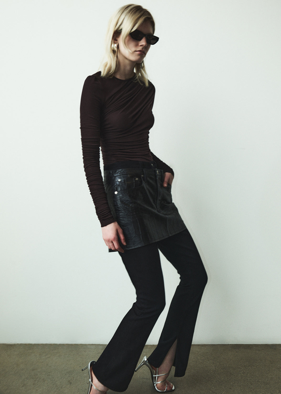 Woman wearing a dark long-sleeve top and black pants against a white background