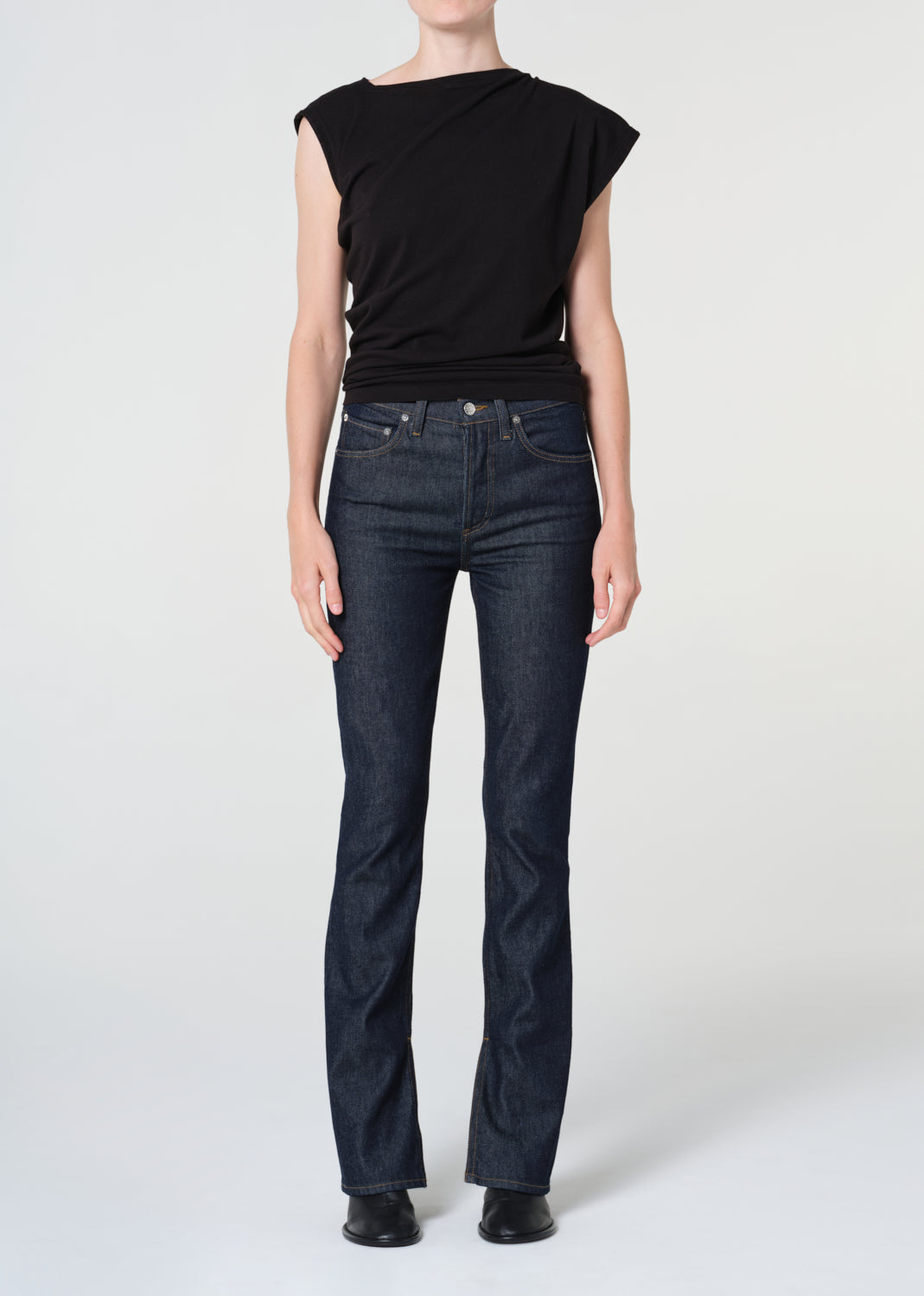Person wearing a black top and dark blue jeans on a white background