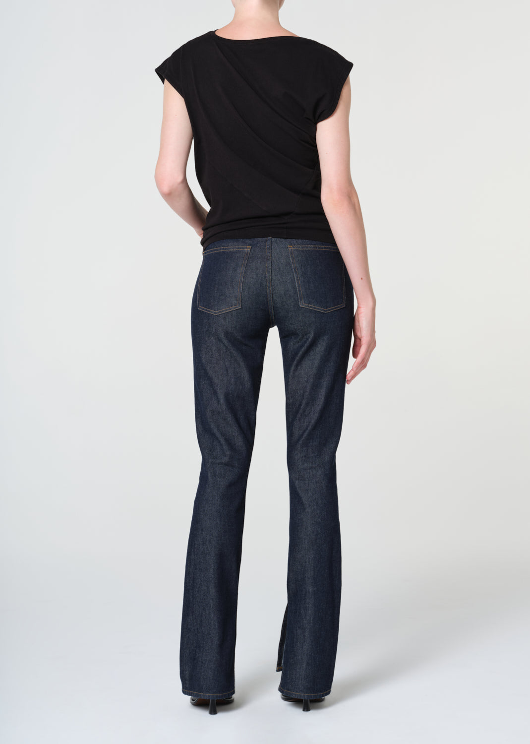 Person wearing a black top and dark blue jeans on a white background