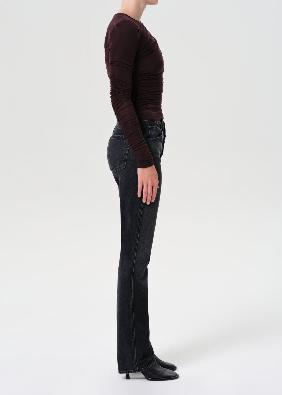 Person wearing a dark brown long-sleeve top and black jeans on a white background