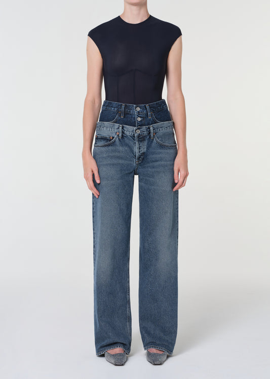Person wearing high-waisted blue jeans and a black sleeveless top on a white background