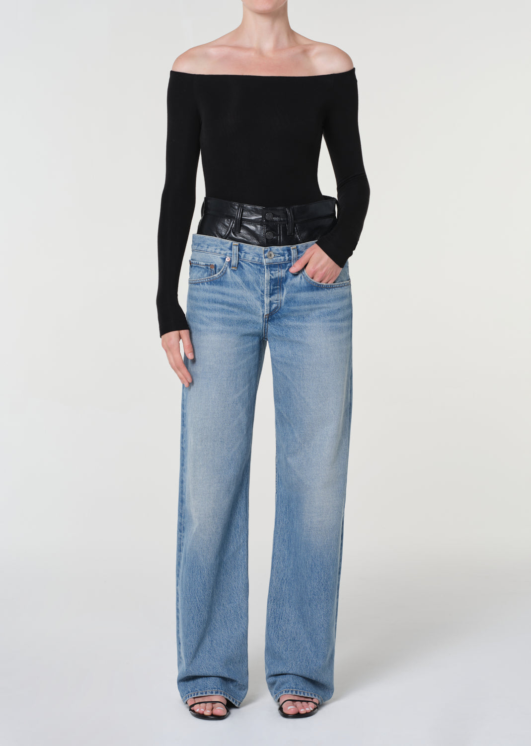 Person wearing a black off-shoulder top and light blue jeans on a white background