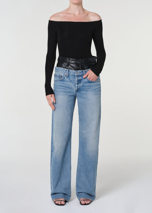 Person wearing a black off-shoulder top and light blue jeans on a white background