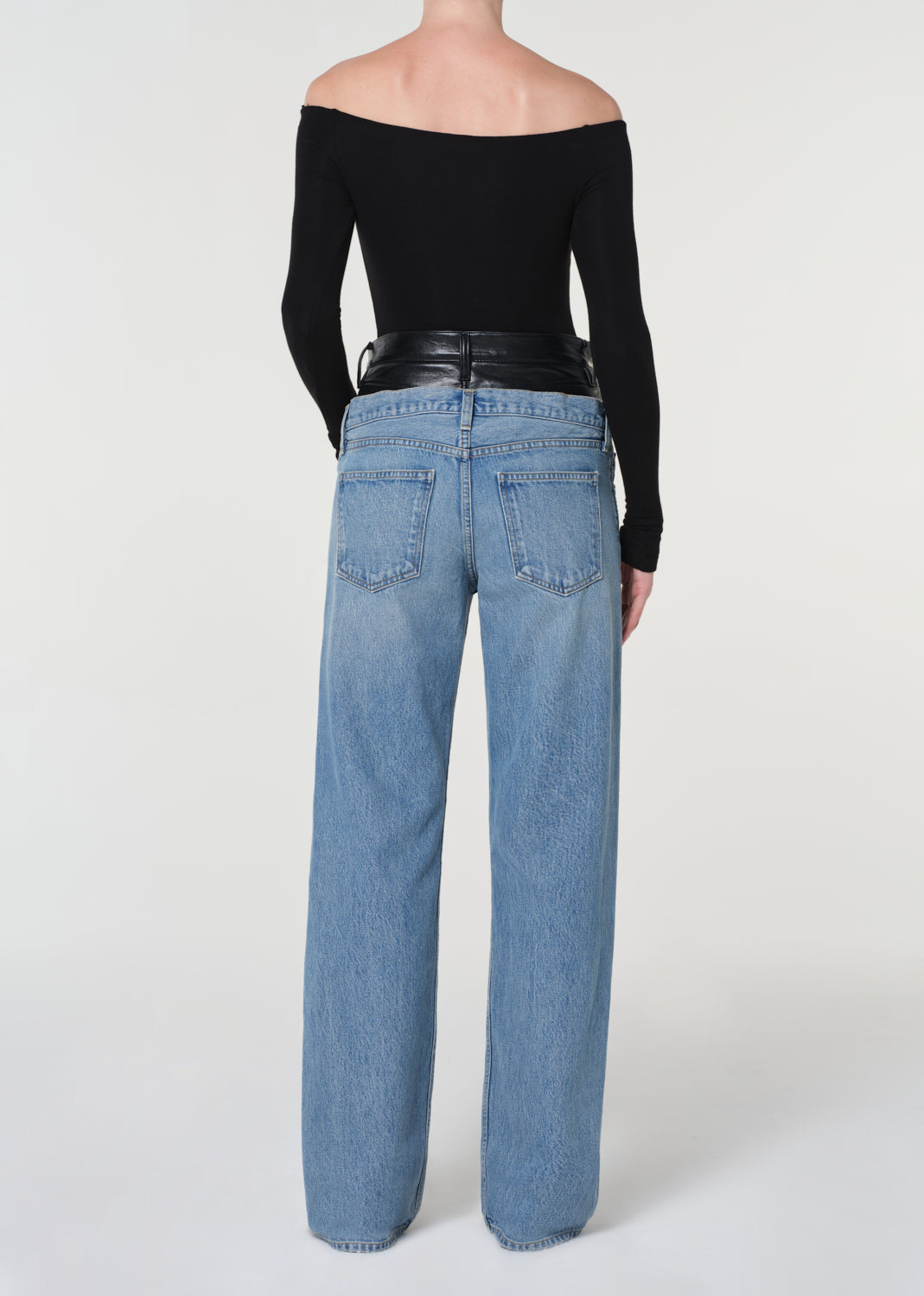 Person wearing blue jeans and a black off-shoulder top on a white background