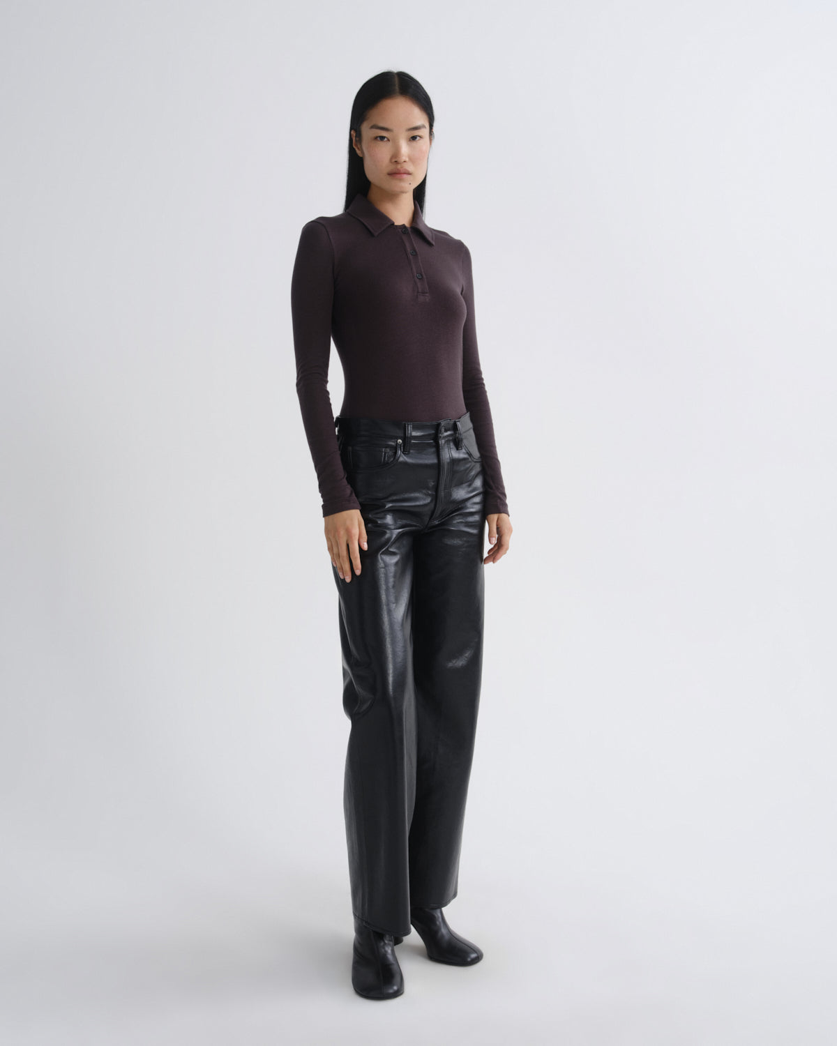 Person wearing a dark long-sleeve top and black leather pants on a white background