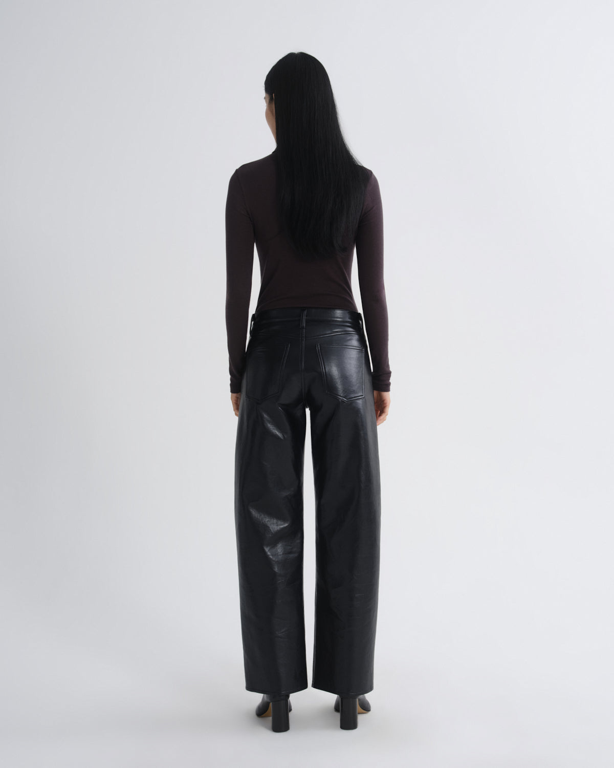 Person wearing black leather pants and a dark top on a white background