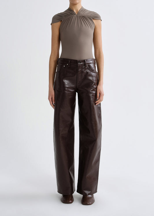 Person wearing a taupe cap sleeve draped top with dark brown leather pants on a grey background.