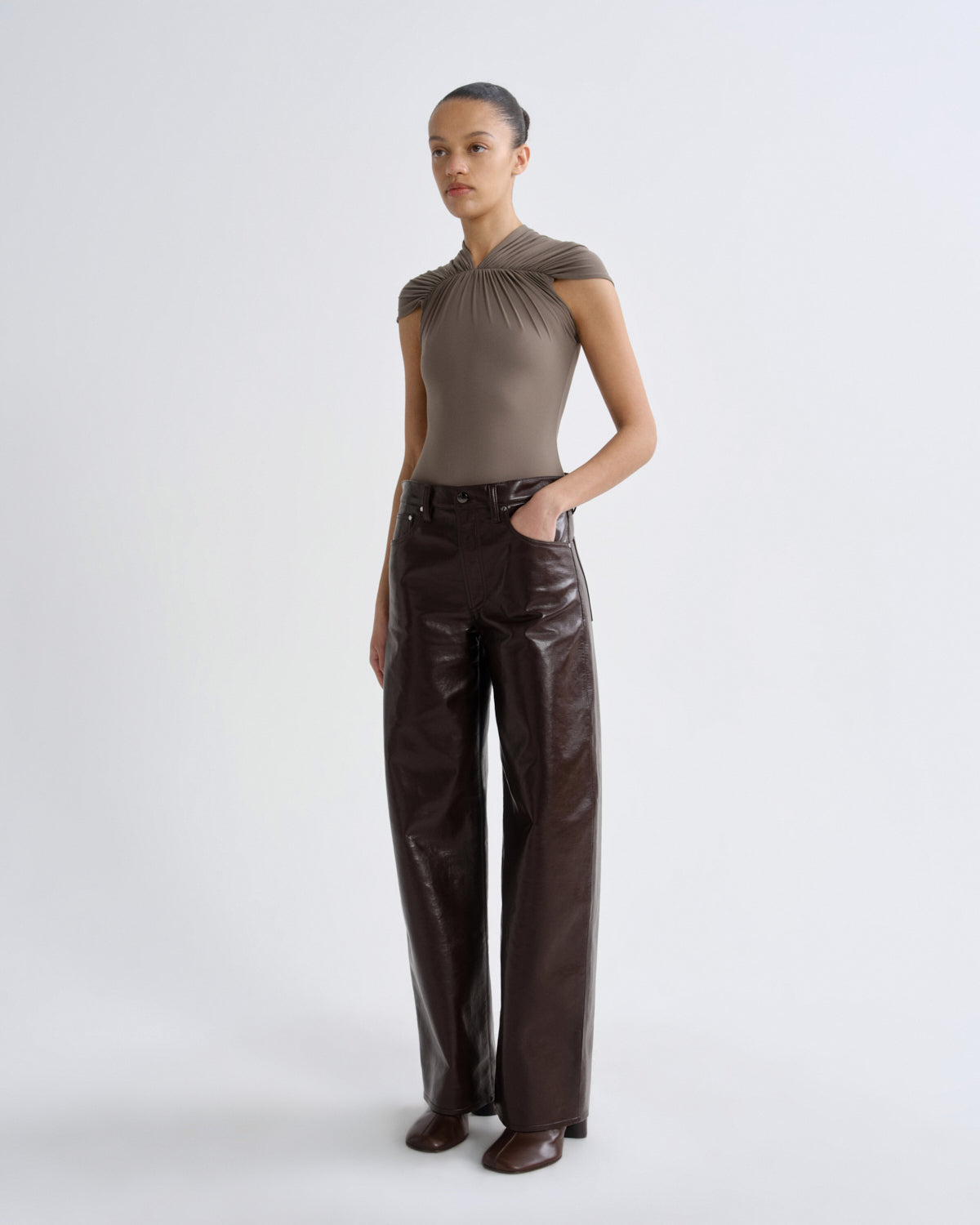 Woman wearing a brown top and shiny black pants on a white background