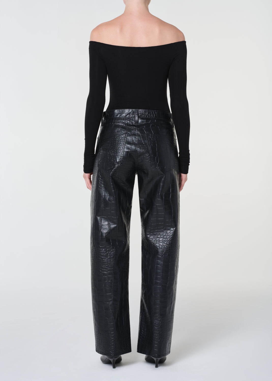 Person wearing black off-shoulder top and shiny black pants on a white background