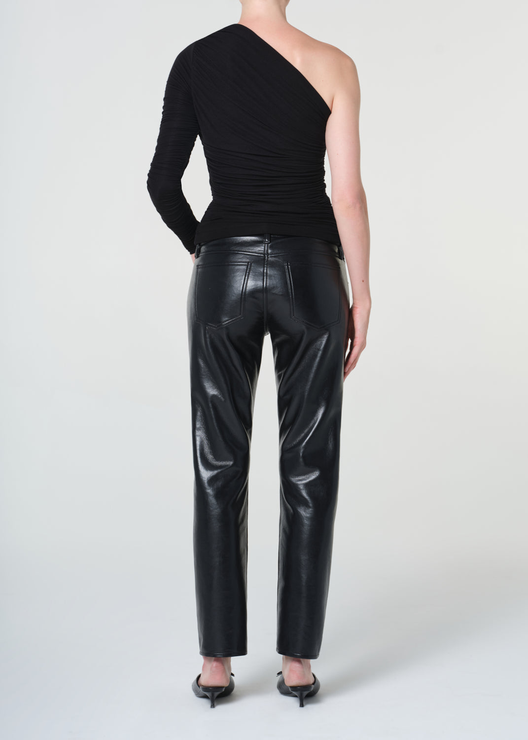 Person wearing a black one-shoulder top and black leather pants on a white background