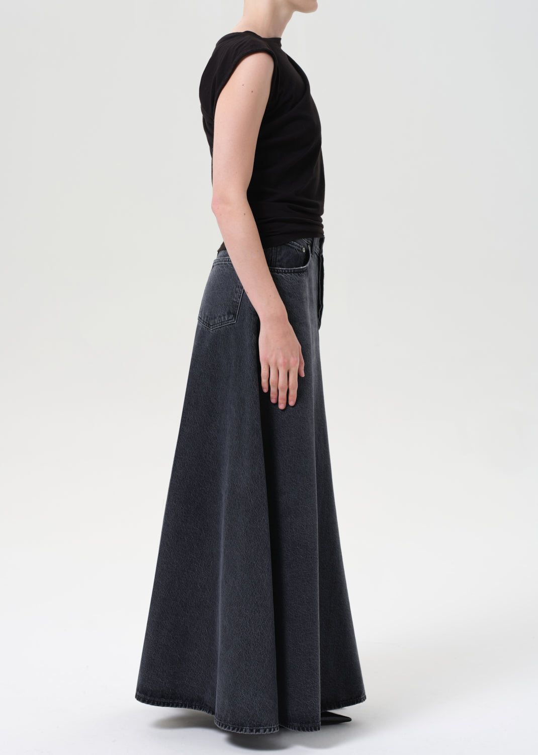 Person wearing a black sleeveless top and long dark gray skirt on a white background
